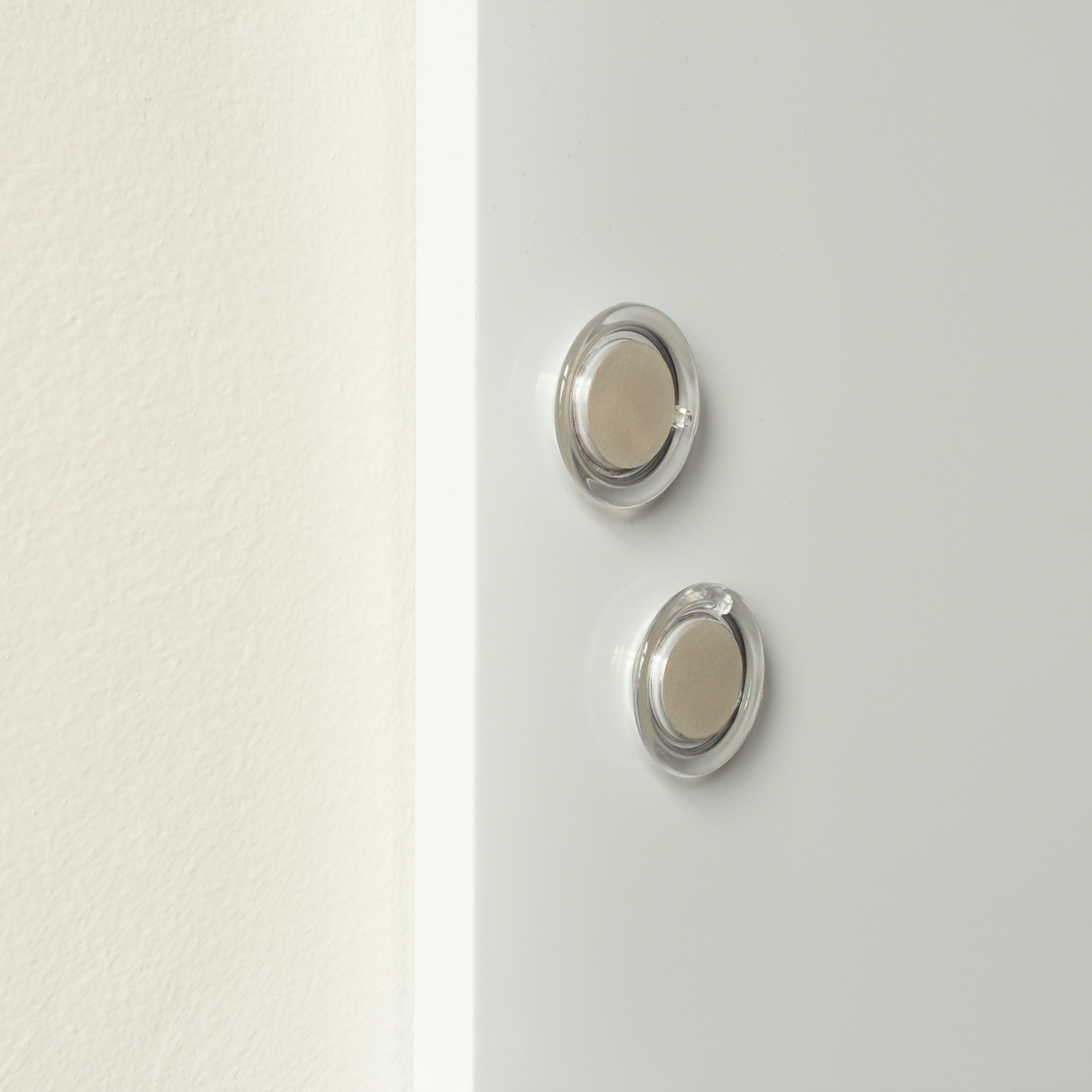 Two round, transparent magnets on a frameless white dry-erase board, highlighting the board's magnetic feature that allows for attaching notes or documents. The simple and clean design is suitable for a variety of settings, from kitchens to offices.